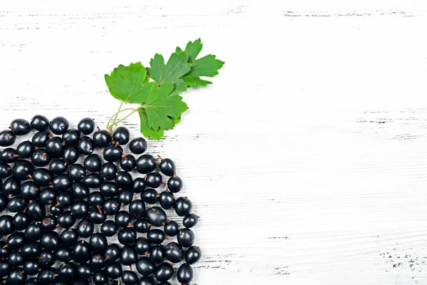 Heap of wild black currant with green leaves on wooden background — Stock Photo, Image