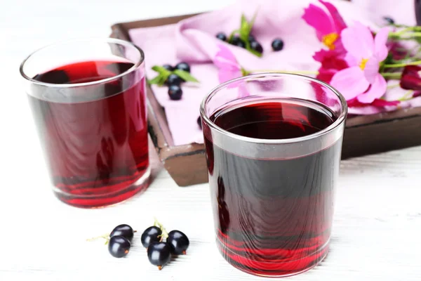 Vasos de jugo de grosella negra fresca en la mesa de madera cerca de la bandeja con flores, primer plano — Foto de Stock