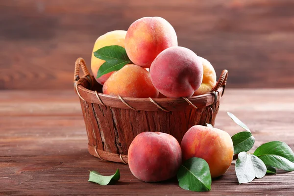 Pesche fresche in cesto di vimini su fondo di legno — Foto Stock