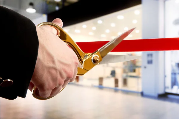 Businessman cutting red ribbon with pair of scissors close up — Stock Photo, Image