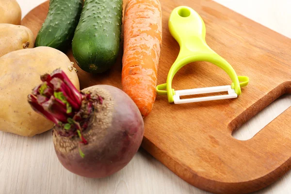 Peeler and raw vegetables on wooden table — Φωτογραφία Αρχείου