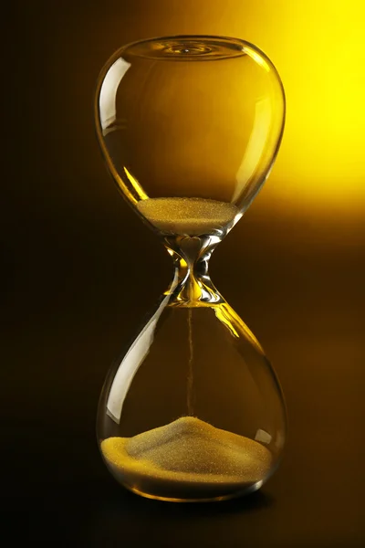 Hourglass on dark yellow background — Stock Photo, Image