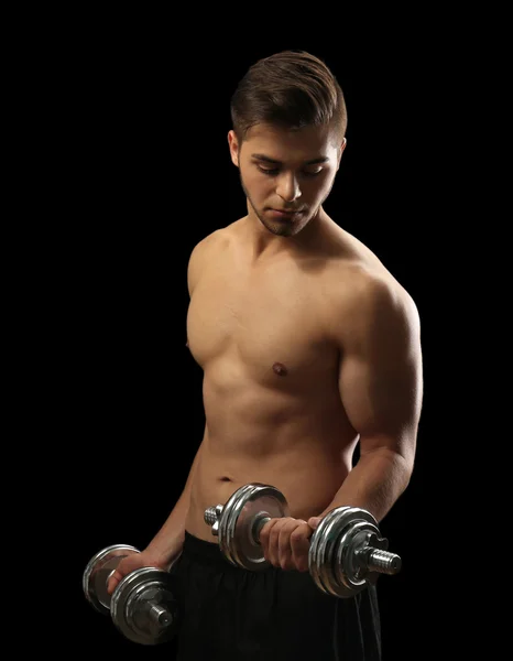 Muscle young man holding dumbbells on dark background — Stock Photo, Image