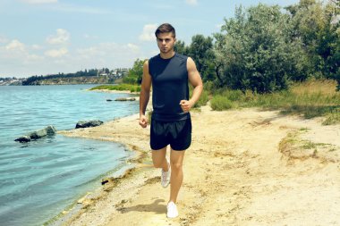 Genç adam sahilde koşuyor.