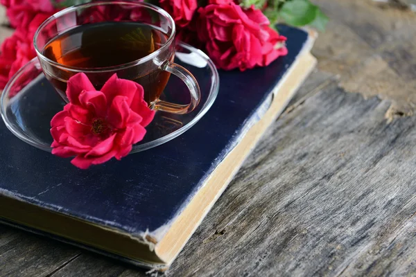 Gammal bok med vackra blommor och kopp te på träbord nära håll — Stockfoto