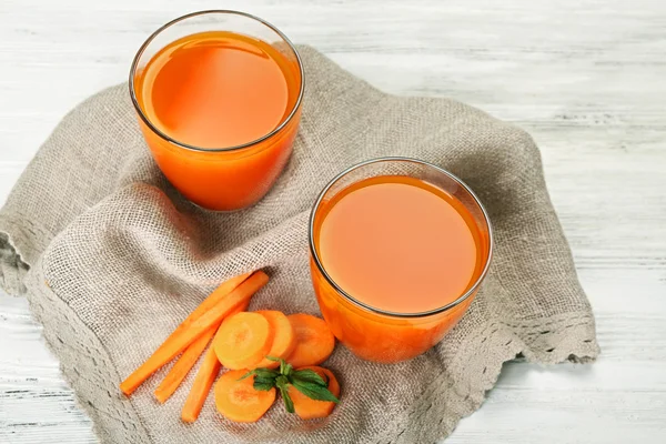 Стаканы морковного сока с овощными ломтиками на столе крупным планом — стоковое фото
