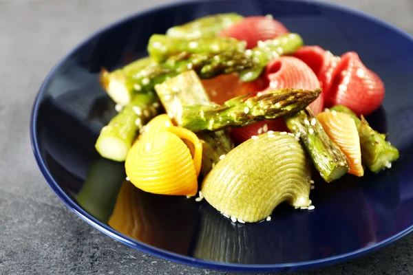 Gebratener Spargel und leckere bunte Pasta mit Gemüse auf Teller auf buntem Hintergrund — Stockfoto