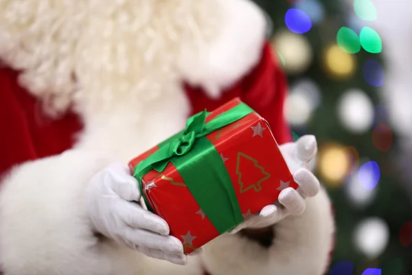 Santa holding gift on Christmas tree — Stock Photo, Image