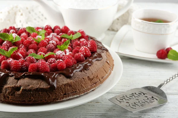 Kuchen mit Schokoladenglasur und Himbeeren und Tasse Tee auf farbigem Holzhintergrund — Stockfoto