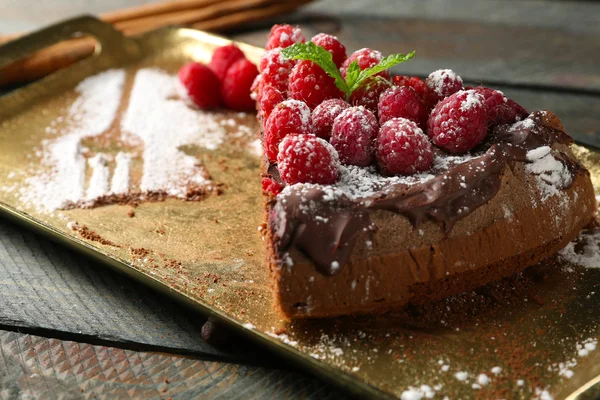 Kuchenstück mit Schokoglasur und Himbeeren auf Blech auf Holzgrund — Stockfoto