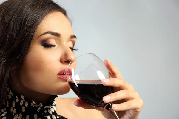 Porträt einer jungen Frau mit einem Glas Rotwein auf grauem Hintergrund — Stockfoto