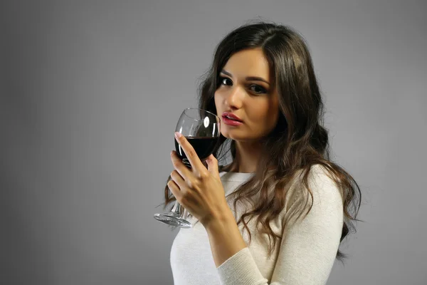 灰色の背景に赤ワインのグラスを持つ若い女性の肖像画 — ストック写真