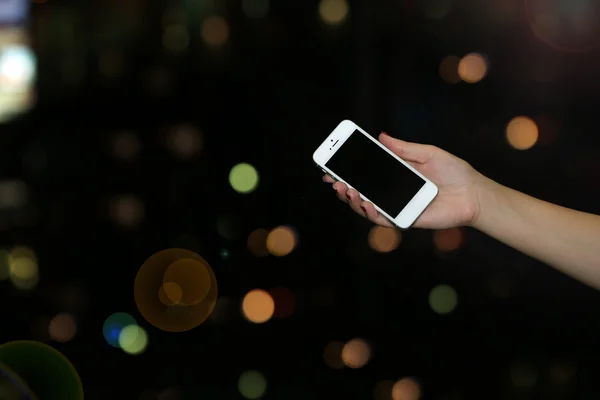Mão feminina segurando tela sensível ao toque telefone celular em luzes noturnas borradas fundo — Fotografia de Stock