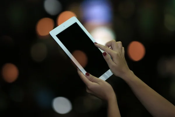 Female hand holding touch screen tablet on blurred night lights background