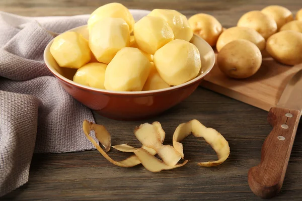 Patatas nuevas peladas en un tazón en una mesa de madera con servilleta, primer plano —  Fotos de Stock