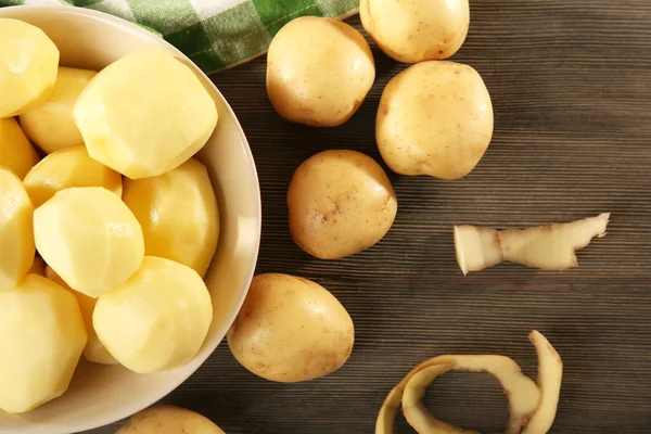 Patate pelate nuove in ciotola su tavolo di legno con tovagliolo, vista dall'alto — Foto Stock