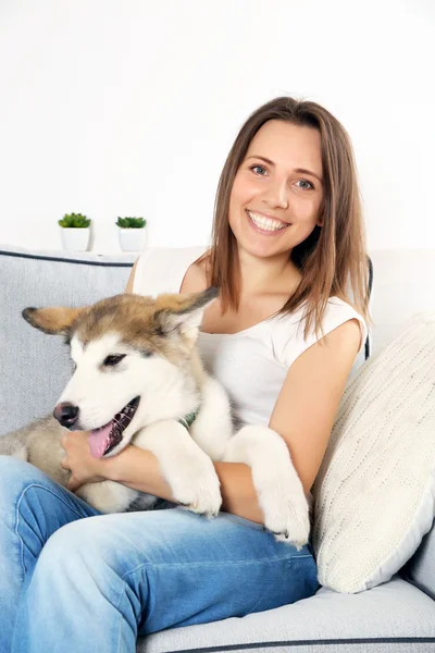 Mulher sentada com seu cão malamute no sofá no quarto — Fotografia de Stock