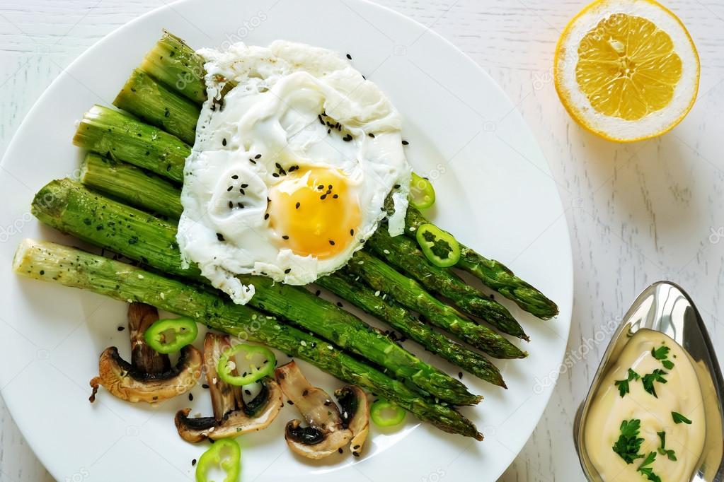 Roasted asparagus with poached egg on plate on table background