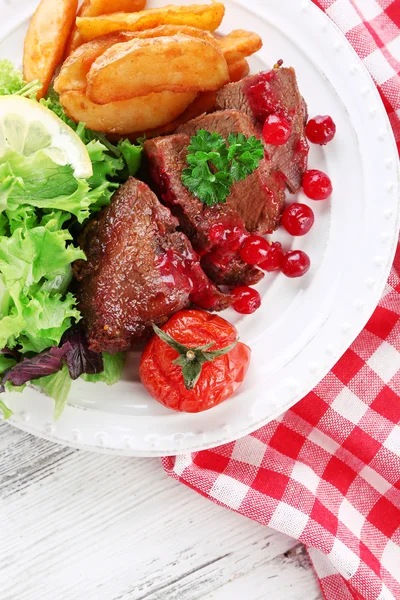 Viande rôtie savoureuse avec sauce aux canneberges et légumes rôtis sur assiette, sur fond de bois de couleur — Photo