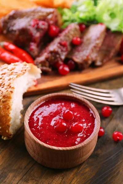 Beef with cranberry sauce, roasted potato slices on cutting board, on wooden background