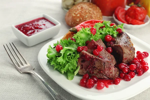 Tasty roasted meat with cranberry sauce on plate, on light background