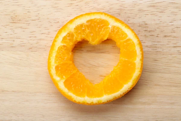 Rebanada naranja con corte en forma de corazón sobre fondo de madera —  Fotos de Stock