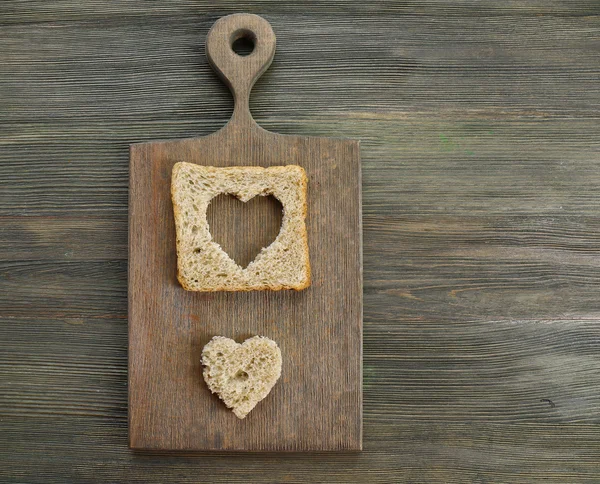 Brotscheibe mit herzförmigem Schnitt auf Holzgrund — Stockfoto