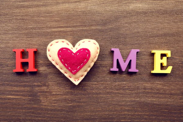 Letras decorativas formando palavra HOME com coração sobre fundo de madeira — Fotografia de Stock