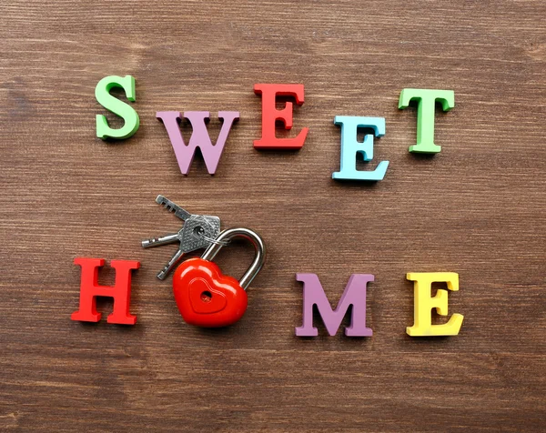 Decorative letters forming words SWEET HOME with lock and keys on wooden background — Stock Photo, Image