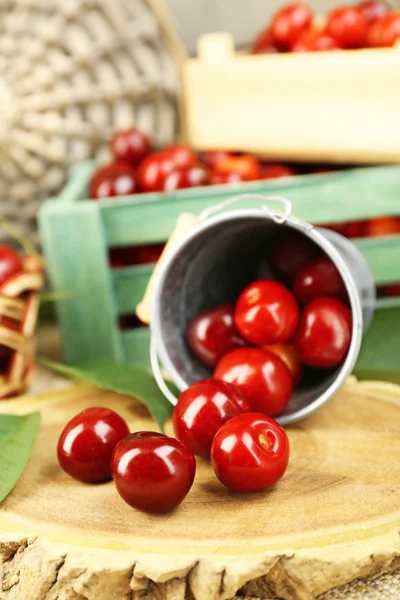 Cerises douces avec feuilles vertes dans un seau et des boîtes en bois, sur fond en bois — Photo