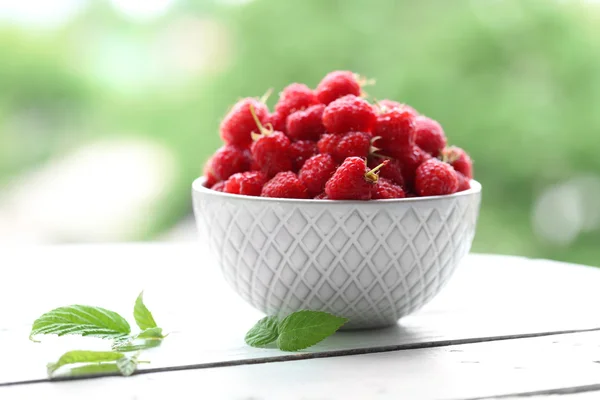 Fresh raspberries in bowl on wooden table on blurred nature background — Stock Photo, Image