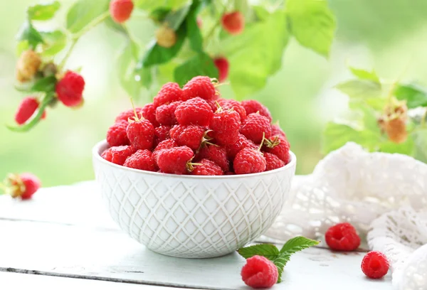 Fresh raspberries in bowl on wooden table on blurred nature background — Stock Photo, Image