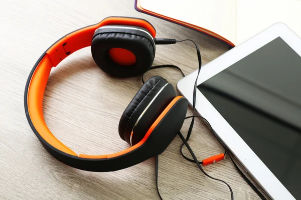 Headphones with tablet and notebook on wooden table close up — Stock Photo, Image