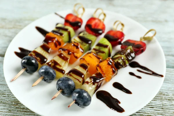 Fresh fruits on skewers in plate on wooden table, closeup — Stock Photo, Image