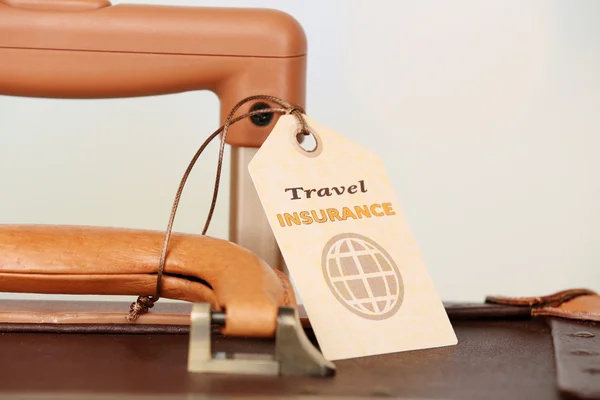 Suitcase with TRAVEL INSURANCE label on light blurred background — Stock Photo, Image