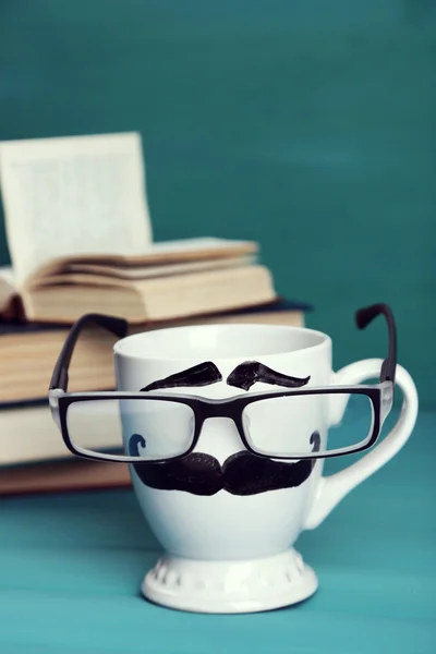 Bücher und Tasse mit Schnurrbart auf buntem Hintergrund — Stockfoto