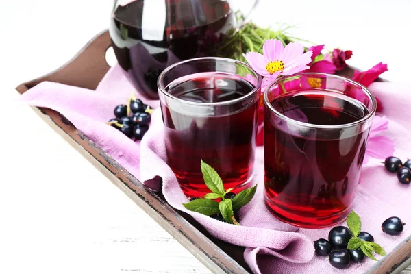 Glasses of fresh blackcurrant juice on wooden tray with pink napkin and flowers, closeup — Stock Photo, Image