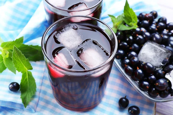 Glasses of fresh blackcurrant juice with ice cubes on checkered napkin, closeup — Stock Photo, Image