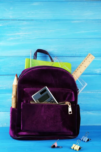 Ryggsäck med skolmaterial på trä bakgrund — Stockfoto