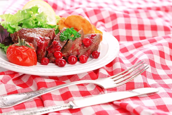 Viande rôtie savoureuse avec sauce aux canneberges et légumes rôtis sur assiette, sur fond de bois de couleur — Photo