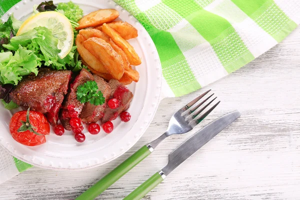 Tasty roasted meat with cranberry sauce and roasted vegetables on plate, on color wooden background — Stock Photo, Image