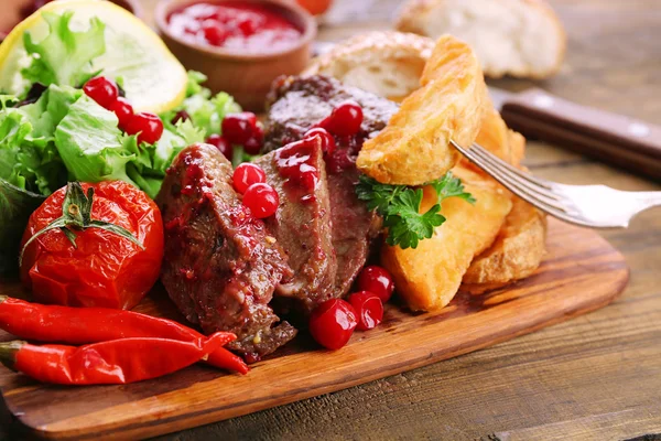 Carne de res con salsa de arándanos, rodajas de patata asadas en la tabla de cortar, sobre fondo de madera —  Fotos de Stock