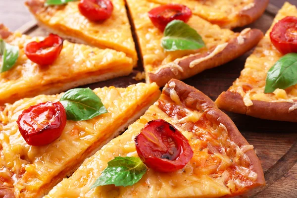 Tranches de délicieuses pizzas au fromage avec basilic et tomates cerises sur la table close up — Photo