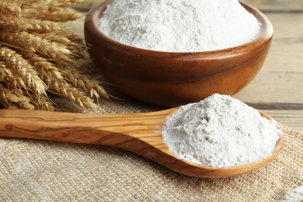 Whole flour in bowl with wheat ears on wooden table, closeup — Stock Photo, Image