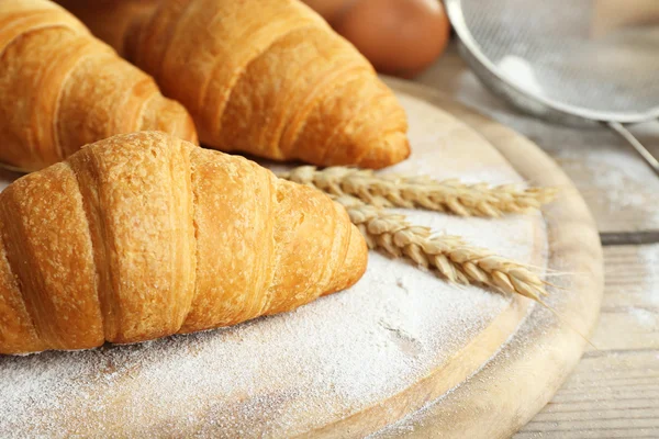 Fresh croissants with flour on wooden table, closeup — Stock Photo, Image