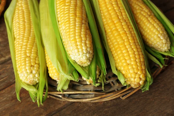 Färsk majs på majskolvar på wicker matta på träbord, närbild — Stockfoto