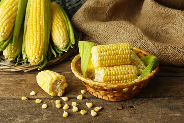 Fresh corn on cobs in wicker bowl on wooden table with sackcloth, closeup — Stock Photo, Image