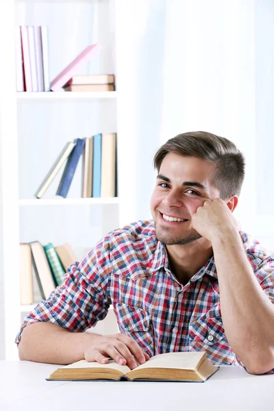 Jovem homem lendo livro à mesa no quarto — Fotografia de Stock