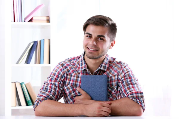 Jonge man leesboek aan tafel op kamer — Stockfoto