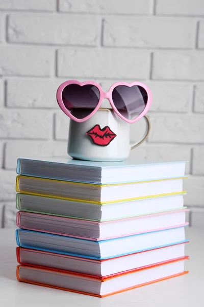 Bücher und Tasse mit Lippen auf Holztisch auf Backsteinwand Hintergrund — Stockfoto
